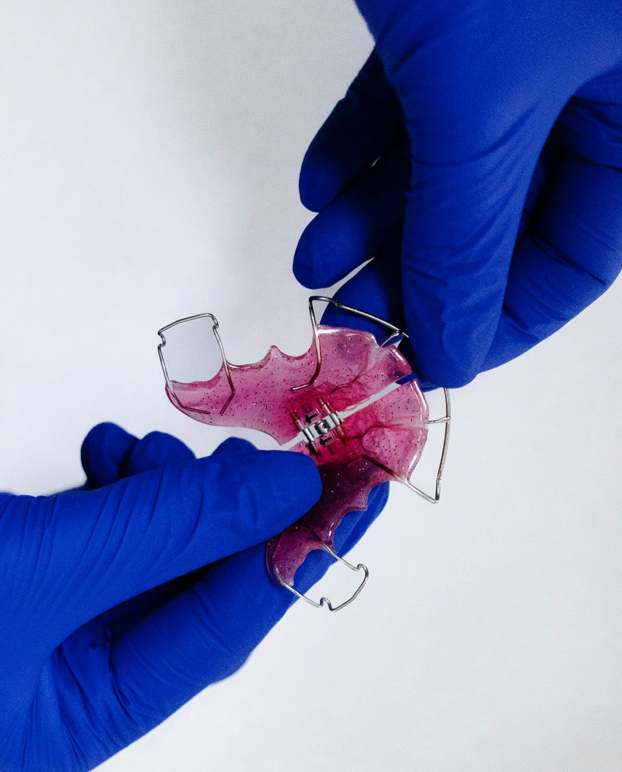 Zwei dunkelblau behandschuhte H&auml;nde halten zeigen eine rosa Nachtzahnspange.